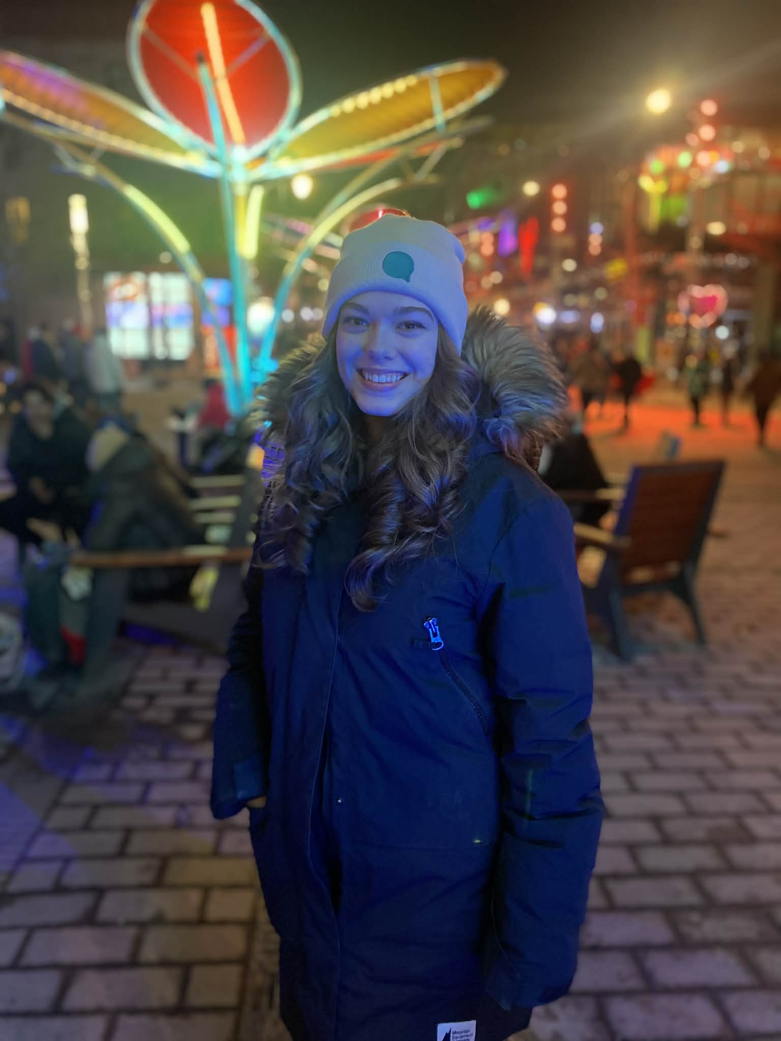 Korinna Gladhill at a winter festival, smiling, with colorful neon lights behind her